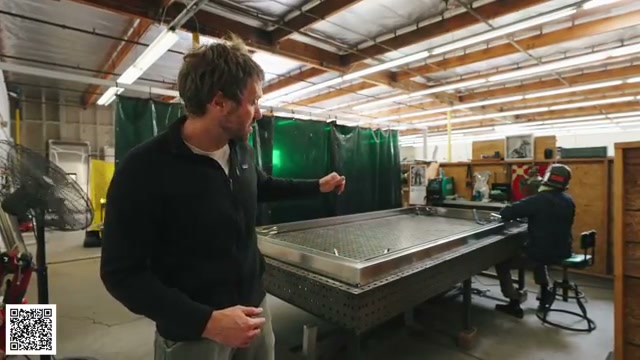 A worker and Thomas examining aluminum pieces held in a welding fixture
