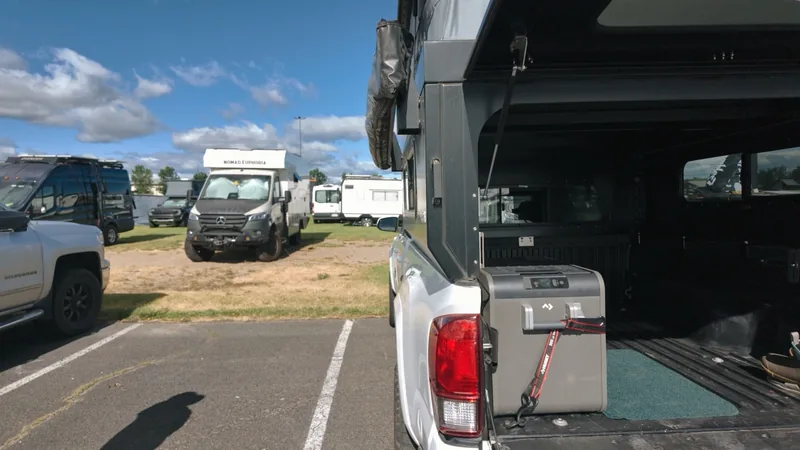 Low view along the truck bed with a grey cooler strapped at the open tailgate; RVs parked across the lot.