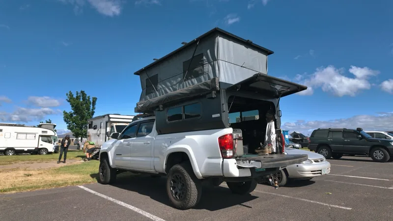 Rear view of the white pickup in a paved lot, camper roof raised, tailgate down and rear hatch open.